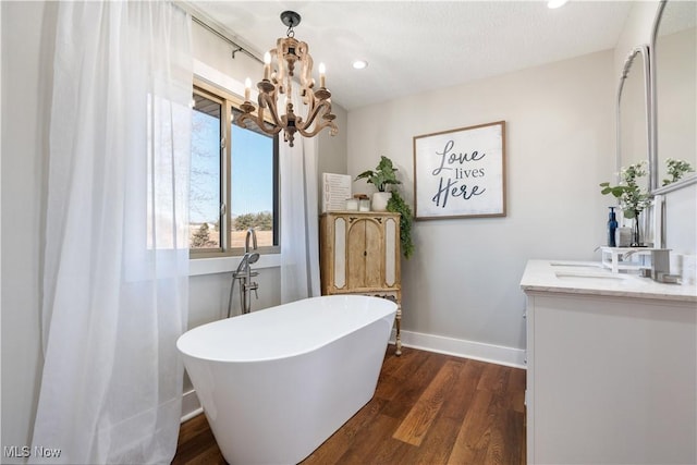 bathroom featuring a chandelier, wood finished floors, vanity, baseboards, and a freestanding bath