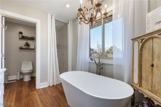 bathroom with baseboards, toilet, wood finished floors, a freestanding tub, and a notable chandelier