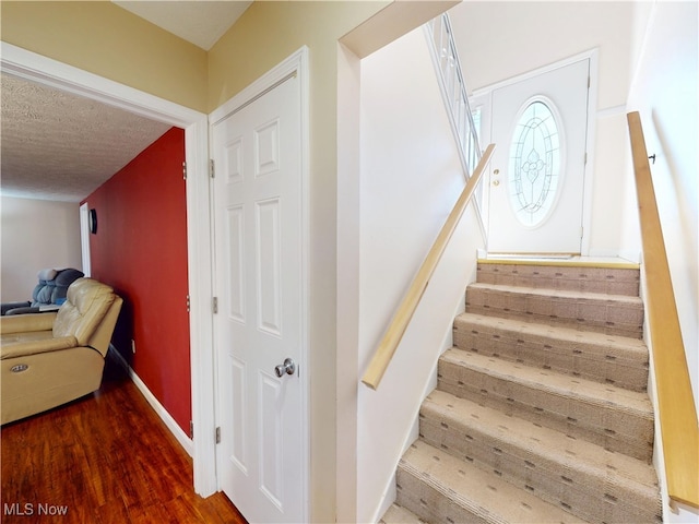 stairway with a textured ceiling, baseboards, and wood finished floors