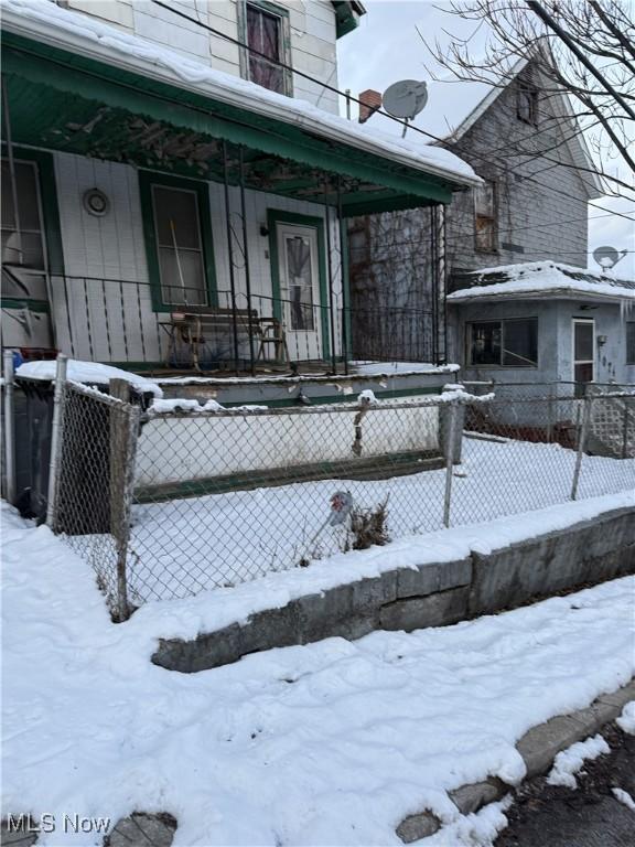 snow covered property entrance featuring covered porch and fence