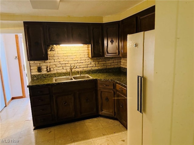 kitchen featuring tasteful backsplash, a sink, freestanding refrigerator, and dark brown cabinetry