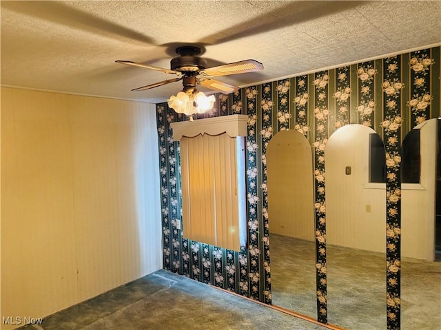 carpeted empty room featuring a textured ceiling, a ceiling fan, and wallpapered walls