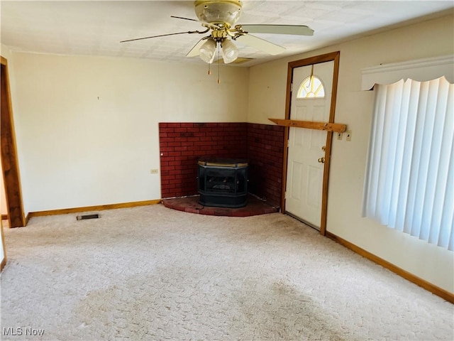 unfurnished living room with baseboards, visible vents, a ceiling fan, a wood stove, and carpet floors