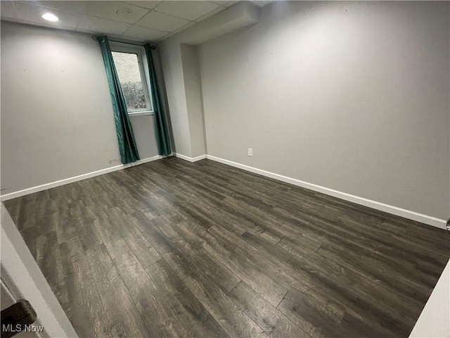 empty room featuring dark wood-style floors, baseboards, and a drop ceiling