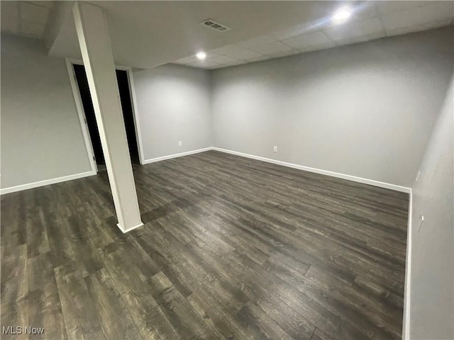 finished basement featuring visible vents, baseboards, a drop ceiling, and dark wood-type flooring