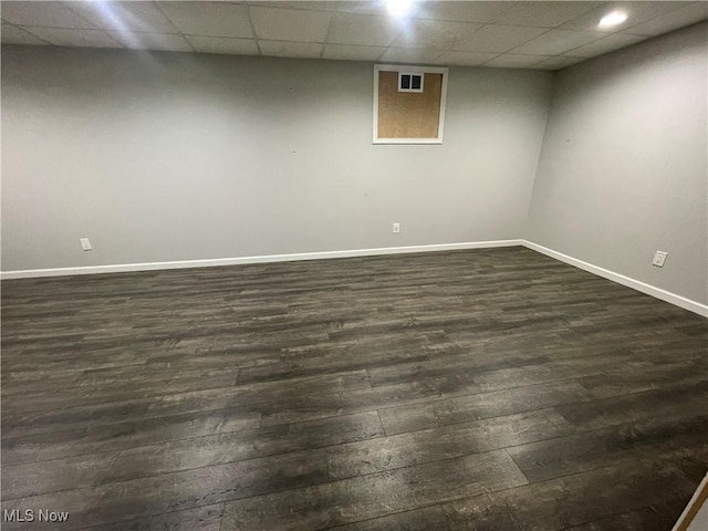 finished below grade area featuring dark wood-style floors, a drop ceiling, visible vents, and baseboards