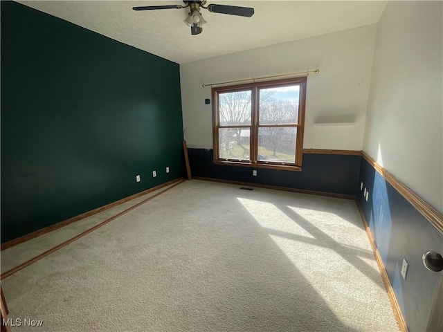 empty room with carpet floors, baseboards, visible vents, and a ceiling fan