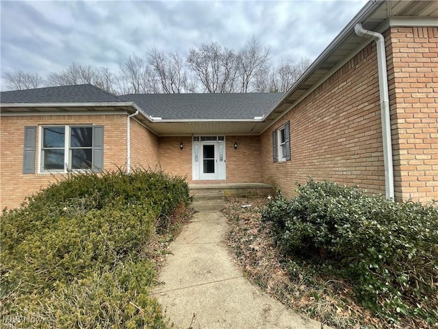 doorway to property with roof with shingles and brick siding