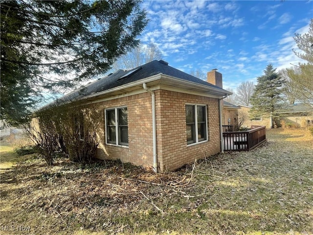 view of side of home featuring roof with shingles, a chimney, and brick siding