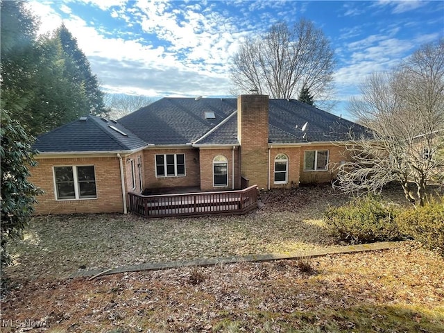 rear view of house featuring a shingled roof, brick siding, a chimney, and a deck