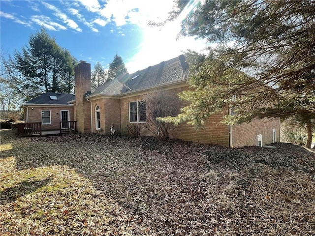 back of house with a deck, brick siding, and a chimney