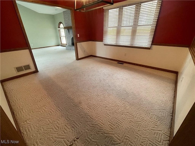 spare room with a brick fireplace, carpet, visible vents, and baseboards