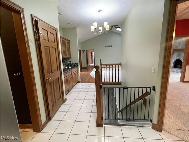 hallway with a notable chandelier, visible vents, light tile patterned flooring, vaulted ceiling, and an upstairs landing