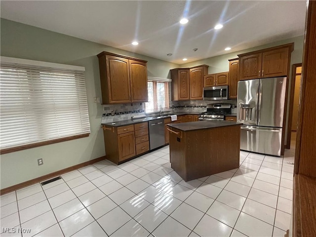 kitchen with light tile patterned floors, decorative backsplash, dark countertops, a kitchen island, and appliances with stainless steel finishes