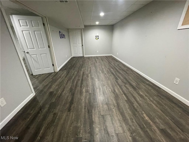 interior space with a paneled ceiling, visible vents, baseboards, and dark wood-style flooring