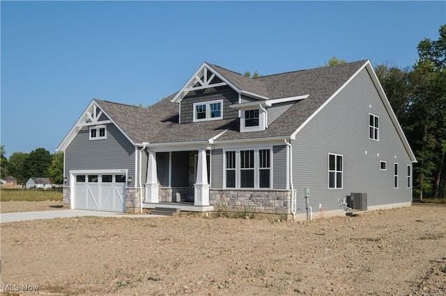 craftsman-style house featuring roof with shingles, concrete driveway, covered porch, central AC unit, and a garage