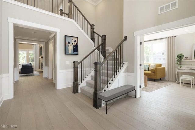 stairs featuring visible vents, a wainscoted wall, ornamental molding, wood finished floors, and a decorative wall