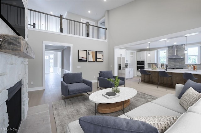 living area featuring light wood-style flooring, a high ceiling, baseboards, and a fireplace with flush hearth