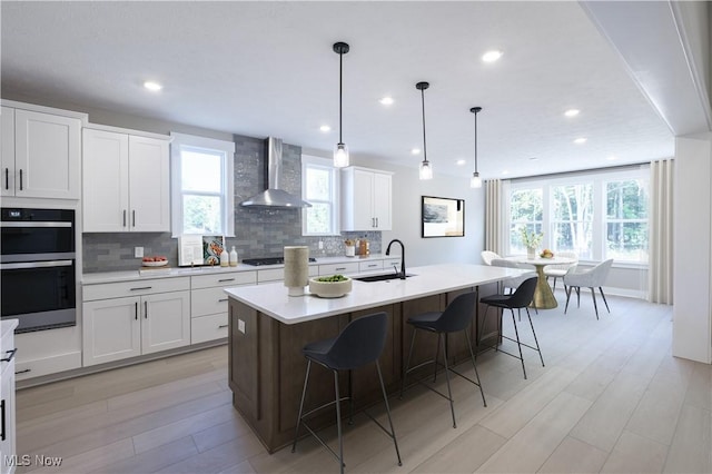 kitchen featuring wall chimney exhaust hood, multiple ovens, a sink, and decorative backsplash