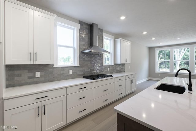 kitchen featuring a sink, gas stovetop, white cabinetry, wall chimney range hood, and backsplash