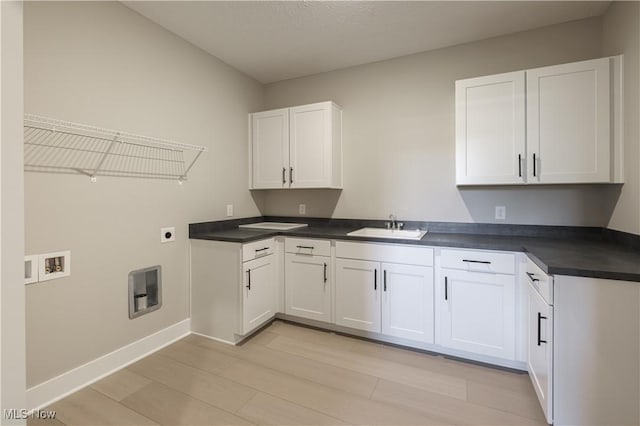 interior space with hookup for a washing machine, a sink, light wood-type flooring, cabinet space, and electric dryer hookup