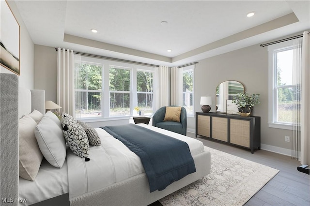 bedroom featuring a tray ceiling, multiple windows, and light wood-type flooring