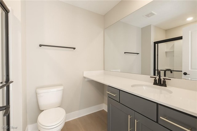 bathroom with toilet, a shower with shower door, vanity, visible vents, and baseboards