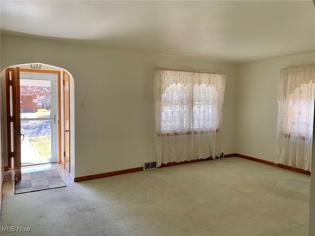 carpeted empty room featuring visible vents, arched walkways, and baseboards