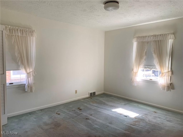 spare room featuring a textured ceiling, carpet, visible vents, and baseboards