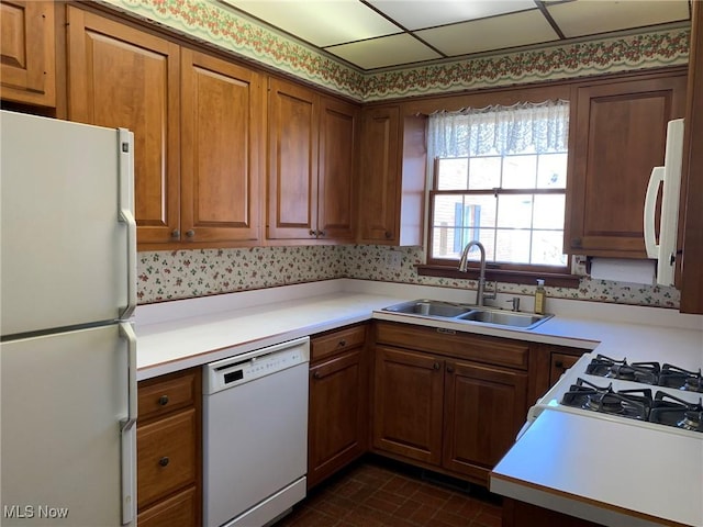 kitchen featuring white appliances, brown cabinetry, a sink, and light countertops