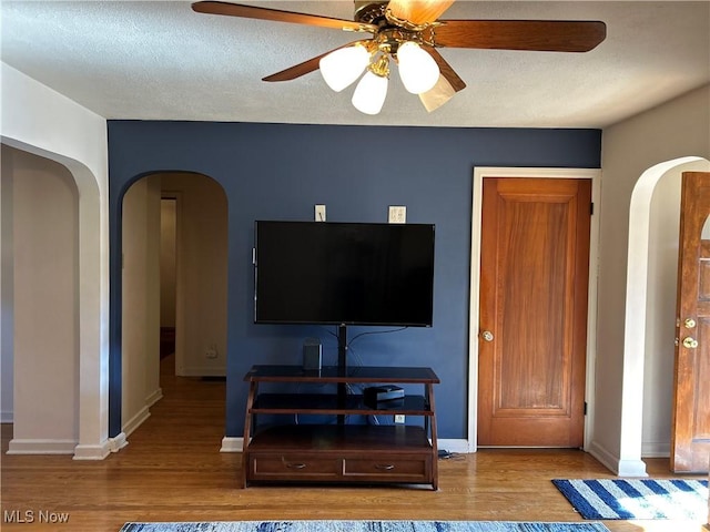 living room with arched walkways, a textured ceiling, baseboards, and wood finished floors