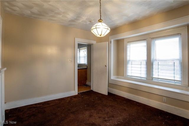 spare room featuring baseboards and dark colored carpet