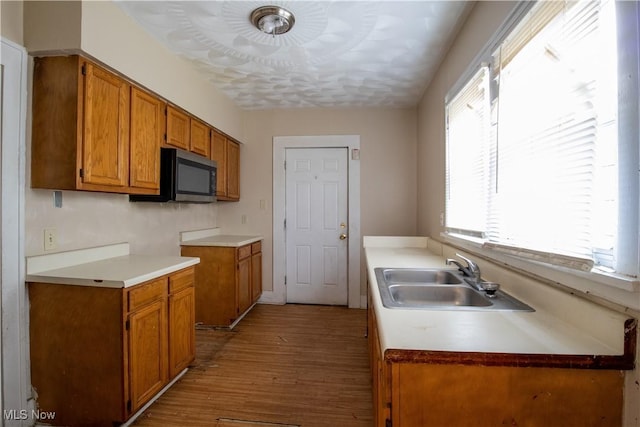 kitchen with stainless steel microwave, brown cabinetry, a sink, and wood finished floors