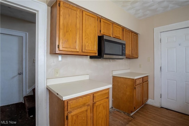 kitchen with brown cabinets, dark wood-style floors, stainless steel microwave, and light countertops