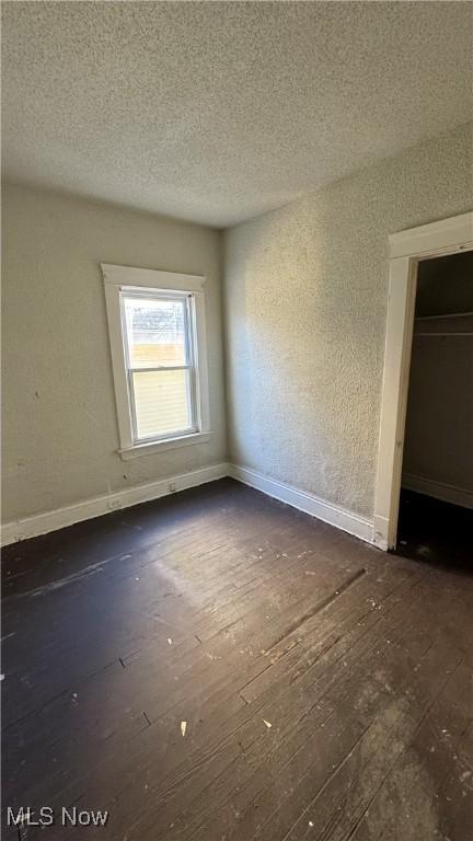 spare room featuring a textured ceiling, dark wood-type flooring, and baseboards