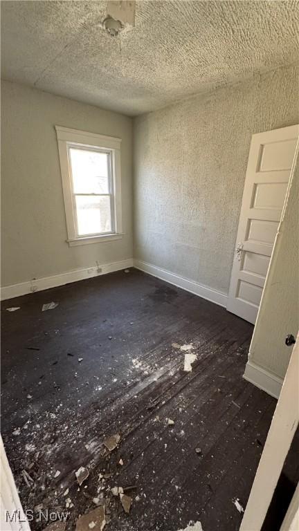 empty room featuring a textured ceiling, baseboards, and wood finished floors