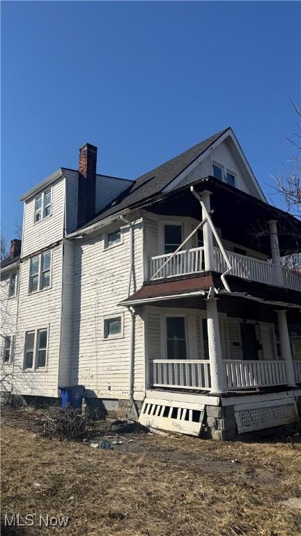 view of side of property featuring a balcony, covered porch, and a chimney