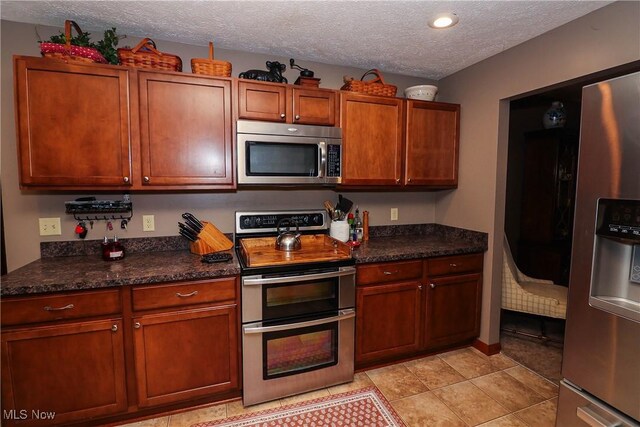 kitchen featuring light tile patterned floors, stainless steel appliances, a textured ceiling, and brown cabinetry