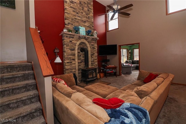 carpeted living room with a wood stove, a healthy amount of sunlight, ceiling fan, and stairway