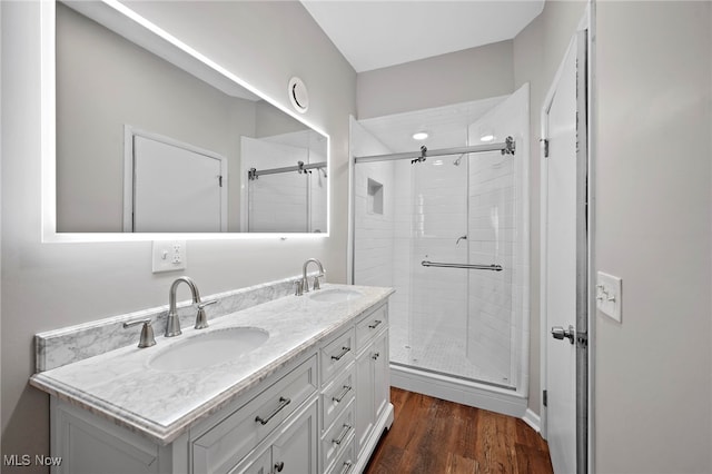 full bathroom featuring double vanity, wood finished floors, a stall shower, and a sink