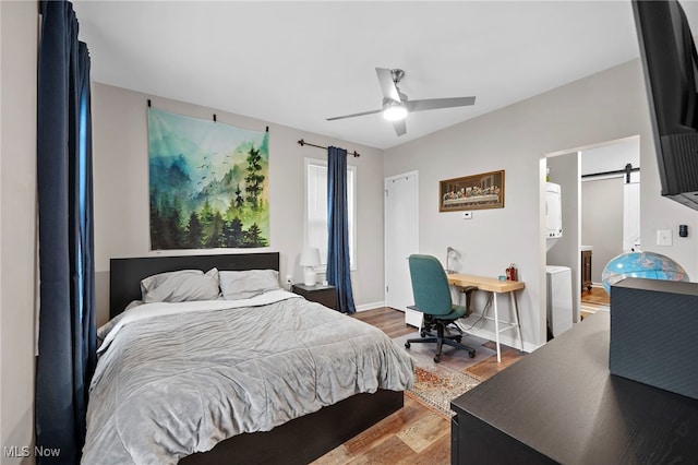 bedroom featuring a barn door, wood finished floors, a ceiling fan, and baseboards