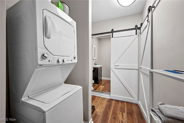 washroom with a barn door, wood finished floors, and stacked washer / drying machine