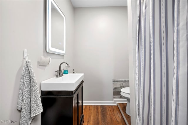 bathroom featuring toilet, a shower with shower curtain, wood finished floors, vanity, and baseboards