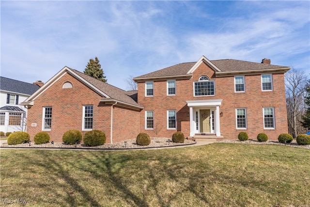 colonial home featuring brick siding, a chimney, and a front yard