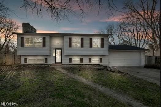 split foyer home with driveway, an attached garage, a chimney, and fence