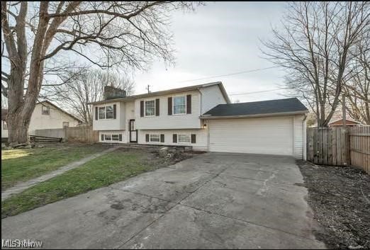 split foyer home featuring driveway, an attached garage, and fence