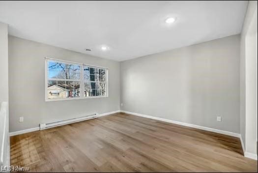 empty room featuring baseboards, a baseboard heating unit, and wood finished floors