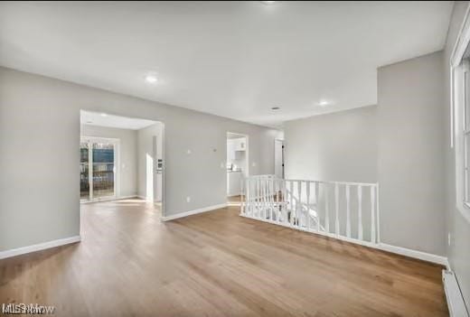 spare room featuring a baseboard radiator, baseboards, and wood finished floors