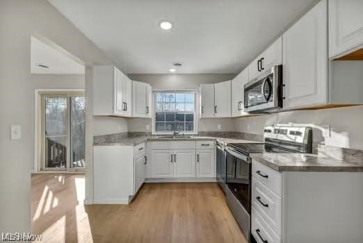 kitchen featuring appliances with stainless steel finishes, a sink, light wood-style flooring, and white cabinetry