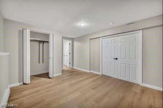 unfurnished bedroom featuring multiple closets, baseboards, and wood finished floors